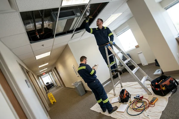 Servicing a ceiling fan coil unit in an office corridor